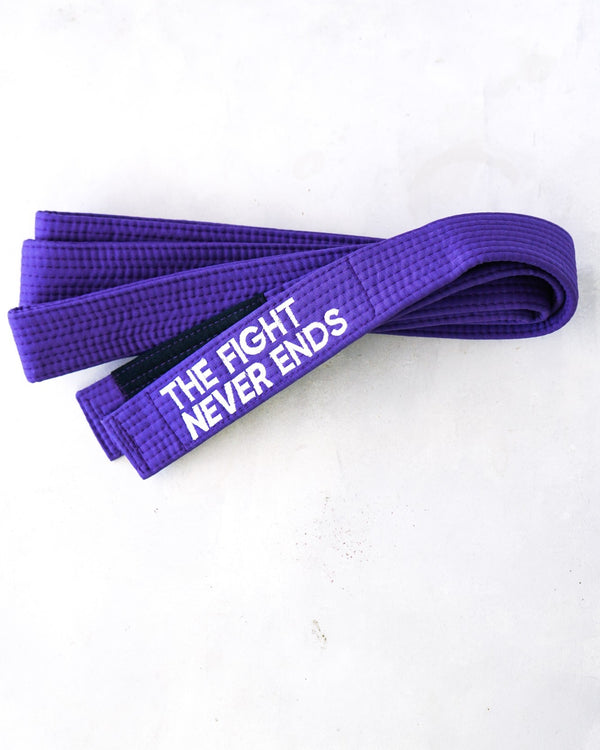 Folded purple BJJ belt on a pale concrete surface