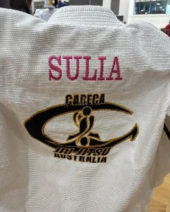 Pink SULIA embroidery above a gold and black Careca Jiu-Jitsu Australia club logo on a white gi back